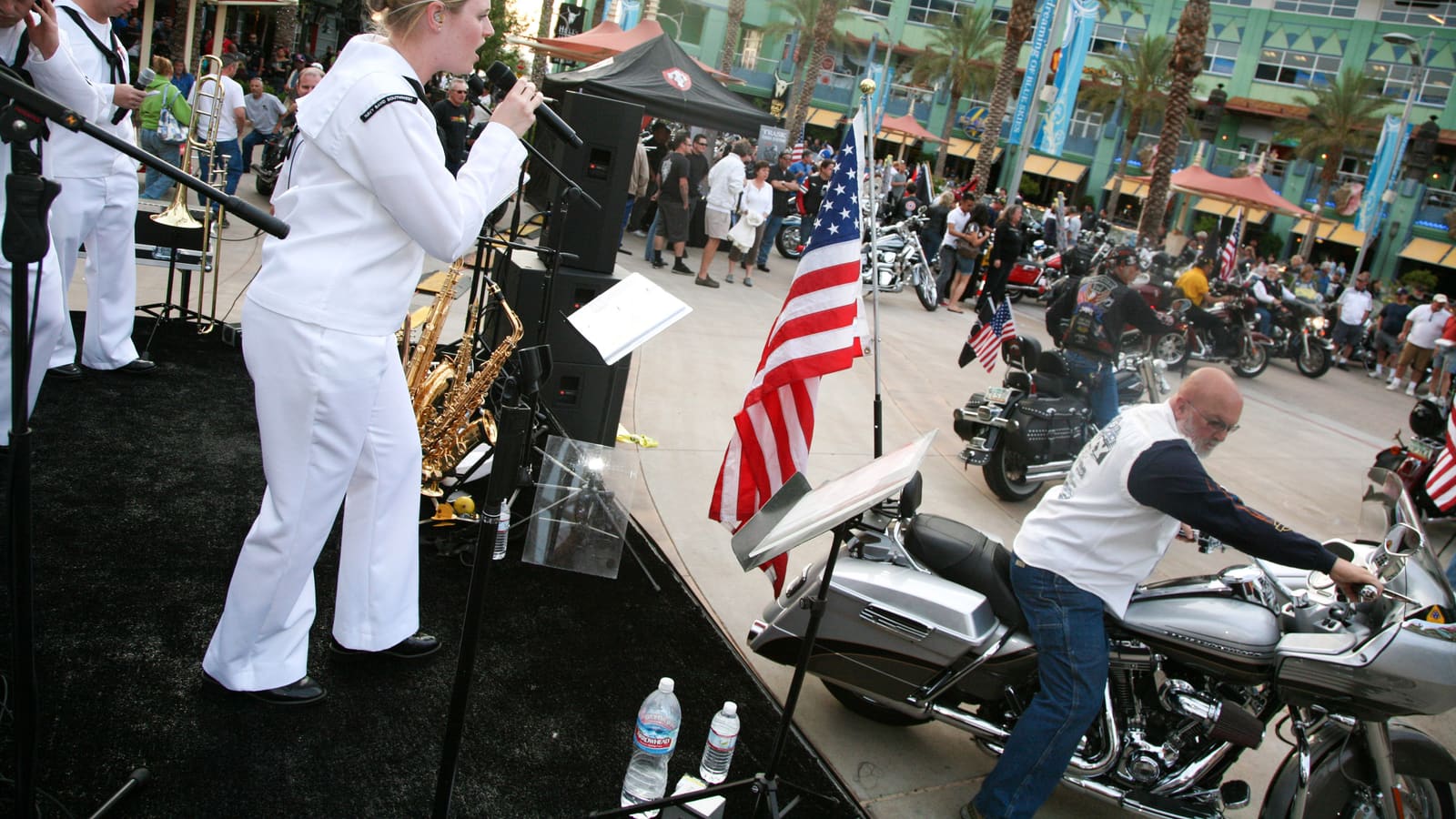 A U.S. Navy Band performs live music on an outdoor stage during a Bike Night event at Westgate Entertainment District in Glendale, Arizona, with a crowd and rows of motorcycles nearby