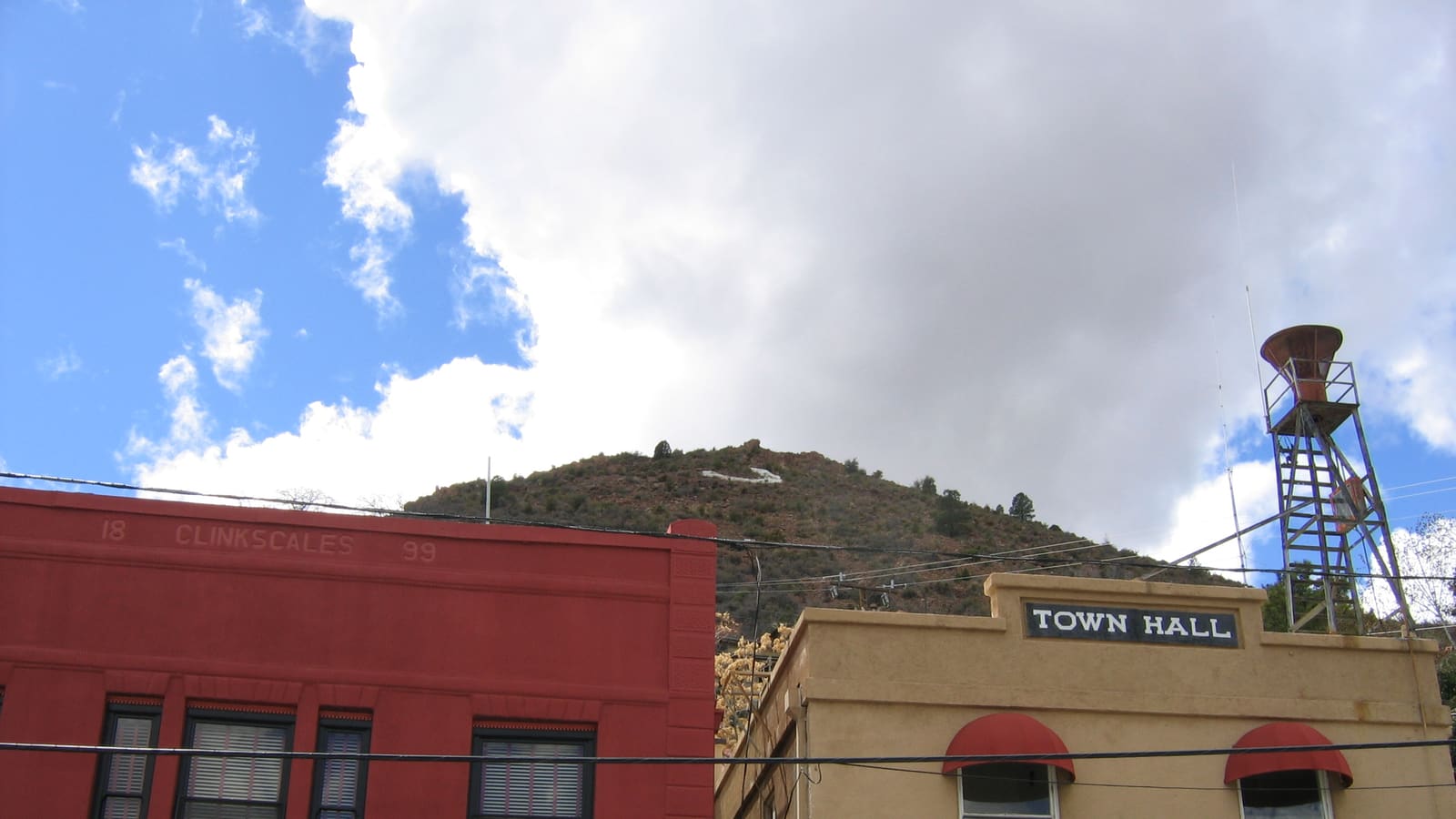 Houses and buildings of Jerome, Arizona stacked along a steep hillside, with the town's large hillside 'J' marker visible on the slope above.