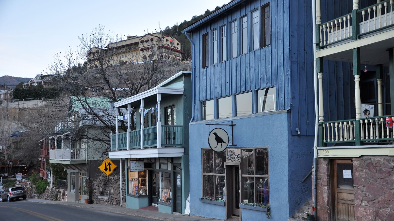 Main Street in Jerome, Arizona, lined with historic storefronts, with the Jerome Grand Hotel visible on the ridge above town.