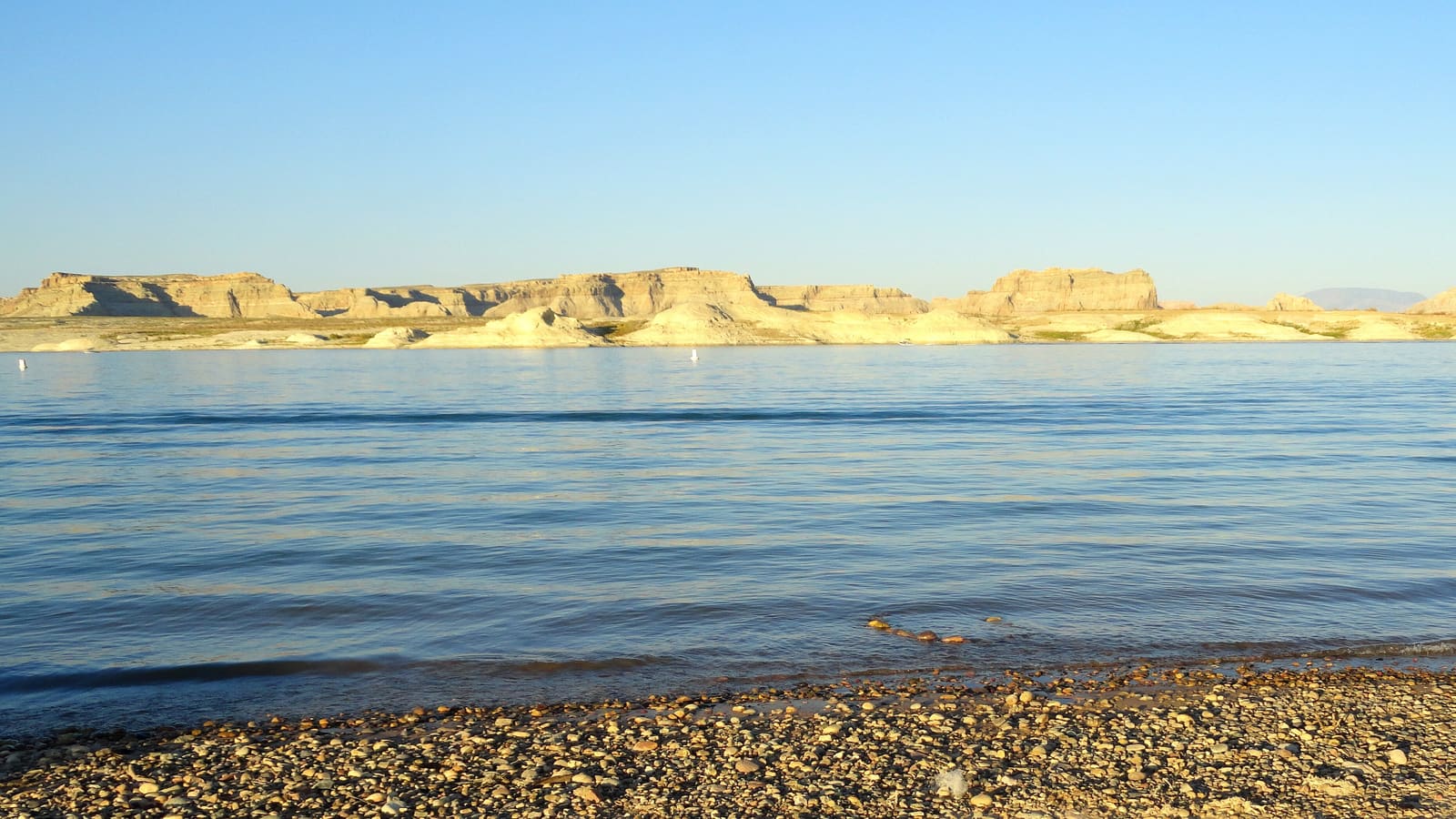 Pebble shoreline of Lake Powell near Page, Arizona, with pale sandstone bluffs across the water