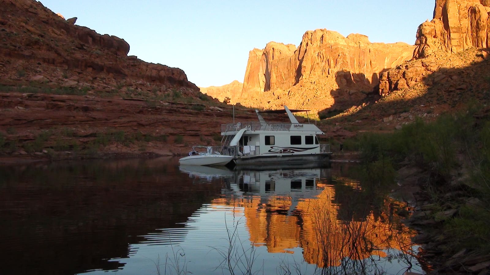 A houseboat moored in a red-rock canyon arm of Lake Powell at sunset