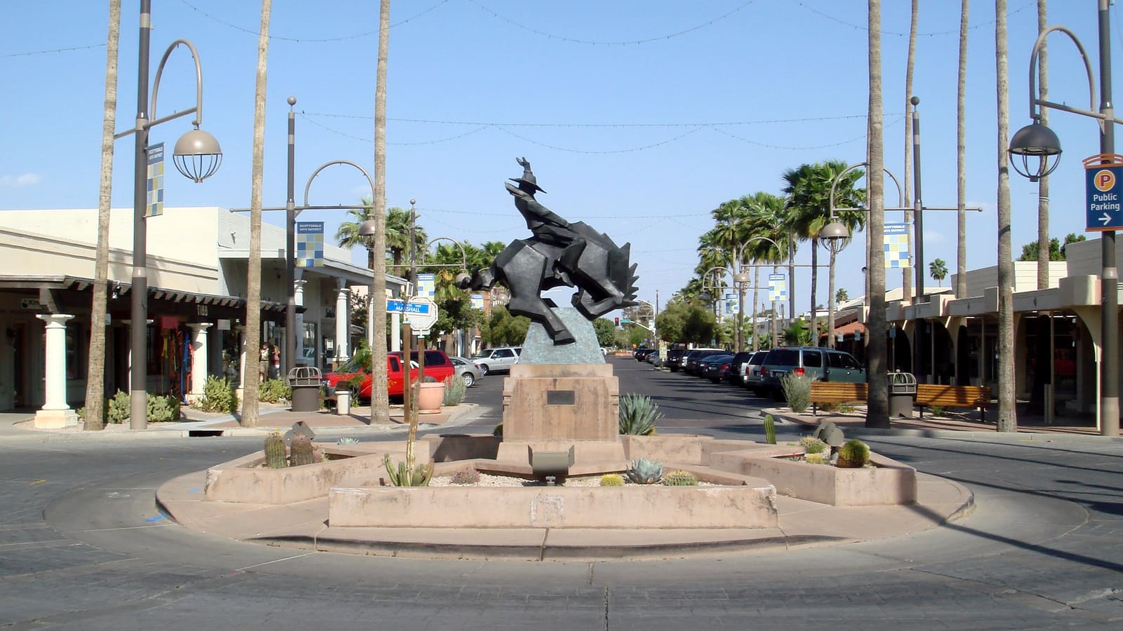 Bronze bucking-horse-and-rider sculpture in a traffic circle on a palm-lined street in Scottsdale's Arts District