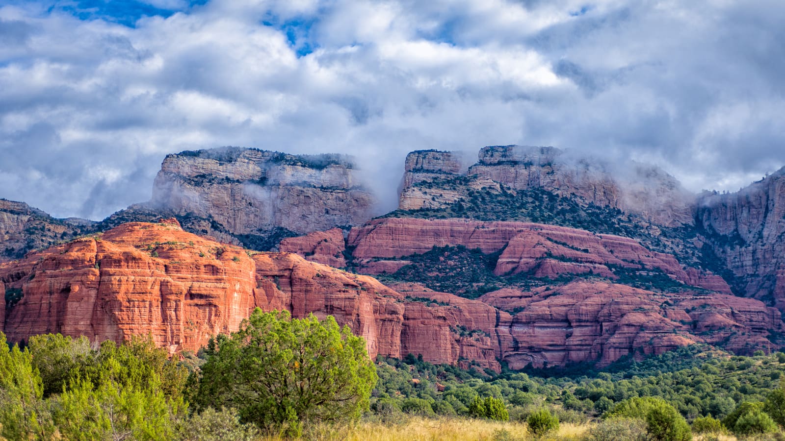 Low storm clouds mixing with red rock bluffs west of Sedona, Arizona, photographed during the region's summer monsoon season.