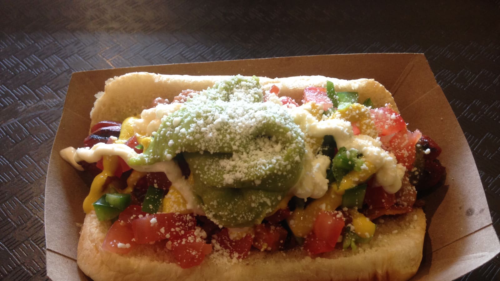 A Sonoran hot dog topped with pinto beans, tomatoes, green salsa, jalapeño, mustard, and mayonnaise